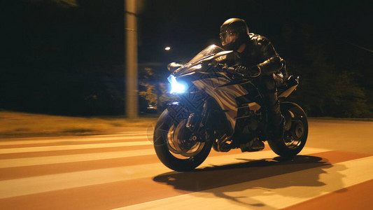 戴着头盔的年轻人在晚上的城市街道上骑着现代黑色摩托车快速骑行摩托车手在夜间空荡的路上赛车他的摩托车驾驶自行车的人自由和爱好背景图片