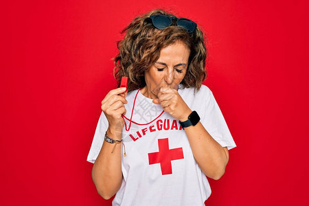 中年期高级夏令营女救生员对红色背景持口哨图片