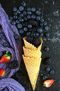 以蓝莓和黑莓在冰淇淋华夫饼圆锥上方的夏季浆果创造平板图景黑暗的创作背景图片