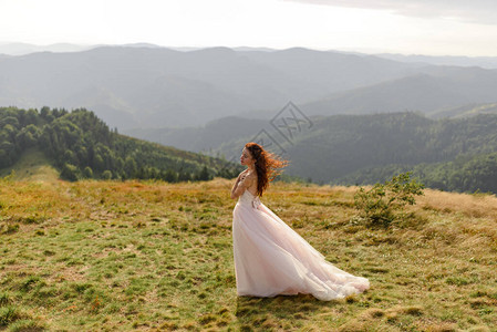 一个美丽的新娘在秋天的山脉背景上的肖像风吹动了她的头发在山顶举行的婚图片