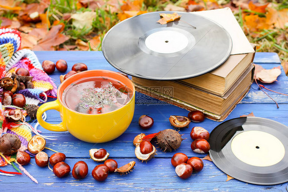 黄色陶瓷杯凉茶和老式黑胶唱片在陈年木制背景上的秋季组合物图片