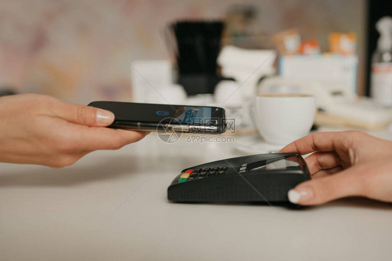 一位女士正准备在咖啡馆里用智能手机通过非接触式NFC技术支付拿铁咖啡的费用一位女咖啡师在咖啡店里拿出一个终端图片