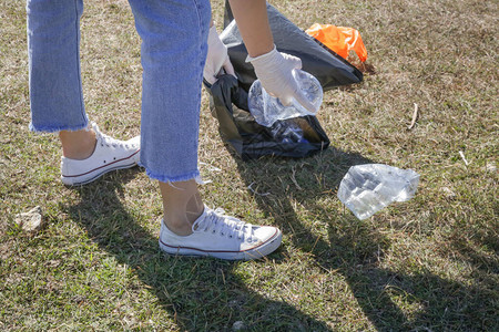 女人从草地上捡起塑料瓶人士收集塑料垃圾的照片志愿者在户外捡起一图片
