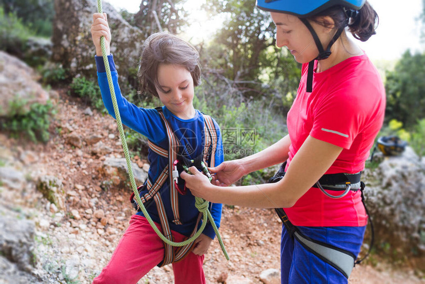 教练孩子使用攀登设备男孩正准备爬岩石一位妇女向孩子展示如何使用登山扣进行保护妈把绳子系图片
