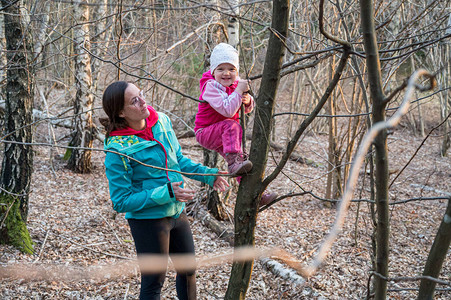 骄傲的活跃母亲帮助她的女儿在森林里爬树促进自然运动和健图片