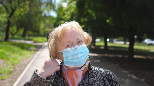 戴着医用口罩的老妇人的肖像站在城市街道上快乐的祖母从COVID19中摘下防护面具图片