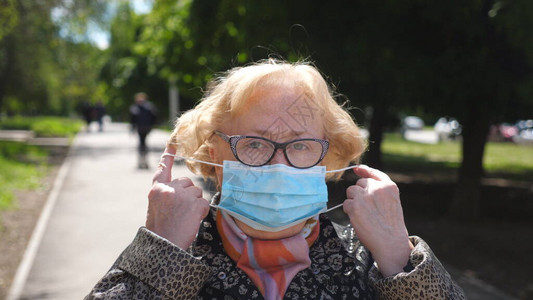 戴着医用口罩的老妇人肖像站在户外戴眼镜的祖母从COVID19中摘下防护面具图片