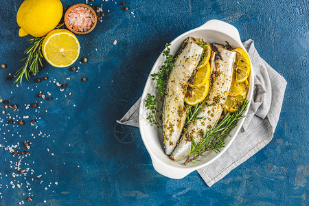 鲭鱼配柠檬百里香迷迭香和料放在白盘上经典蓝色表面上的生腌背景图片