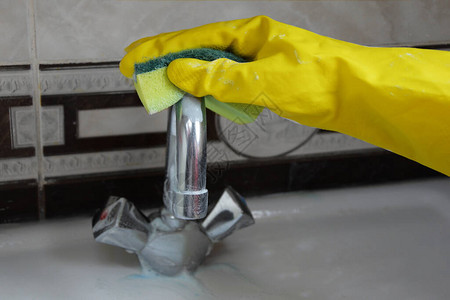 一只戴着黄色橡胶手套的女手正在清洁浴室的水龙头图片