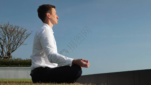 身穿白衬衫的年轻商人在阳光下坐在酒店露台上以莲花姿势冥想图片
