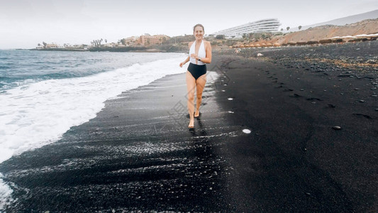 Beautfiul微笑着穿泳衣的年轻女子在海边用黑色火山背景图片