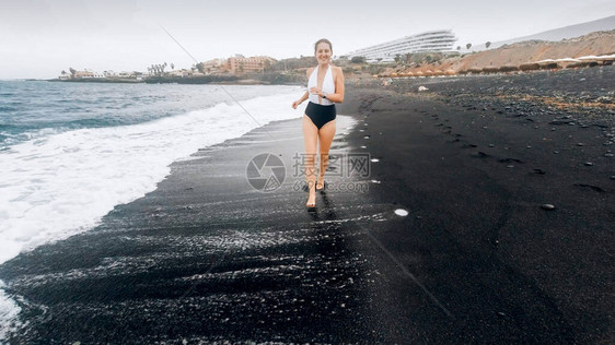 Beautfiul微笑着穿泳衣的年轻女子在海边用黑色火山图片
