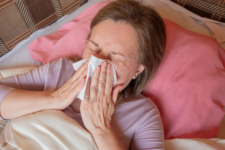 女人打喷嚏流鼻涕或季节过敏40岁的中年妇女躺在床上图片
