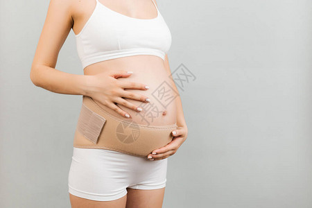 穿着内衣的孕妇在灰色背景和复制空间使用孕带图片