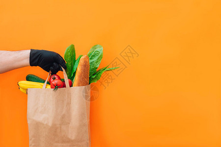 戴着防护手套的快递员的手在橙色背景上运送不同食物的纸袋爆发期间的食品图片