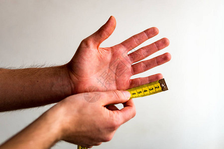 用黄色卷尺测量左手小指的人白色背景橄榄色肤图片
