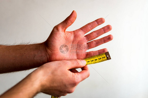 用黄色卷尺测量左手小指的人白色背景橄榄色肤图片