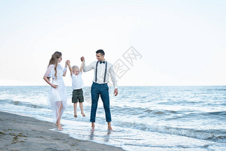 年轻的父母带着儿子在沙滩上散步爸妈牵着宝的手图片