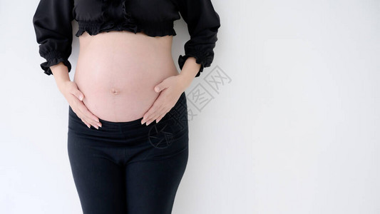 身着黑衣服手握着肚子的孕妇在白墙背图片