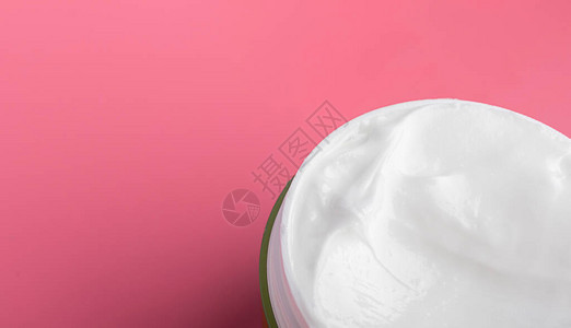 白色面部润滑剂奶油在粉红色背景的圆罐中孤立的宏观脸部和图片