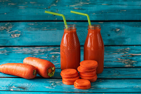 在明亮的蓝色背景上鲜榨胡萝卜汁维生素A胡萝卜素和视黄醇的来源玻璃瓶中的健康蔬菜冰沙素食和素食图片