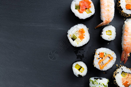 聚餐米饭典型的亚洲美食设置在黑色厨房石板上寿司futomaki和握寿司生鱼片配米饭和蔬菜复背景