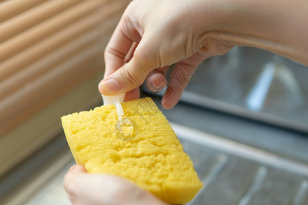 女人在黄色海绵上使用洗碗液关闭管家在水槽里洗脏盘子家政和日常家庭作业概念图片