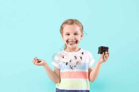 穿脏衣服的小女孩在颜色背景上吃巧克力蛋糕图片