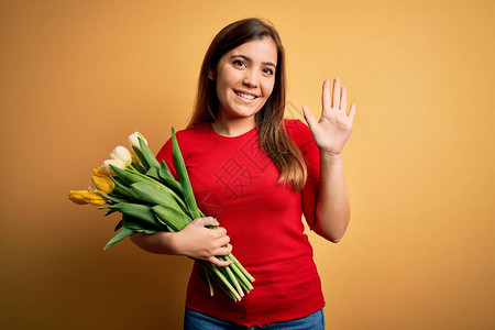 年轻的金发女子在黄色背景上拿着浪漫的郁金香花束放弃打招呼快乐微笑友图片
