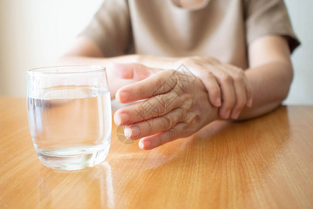 老年妇女的手颤抖症状在木板上为一杯水而伸出手来图片