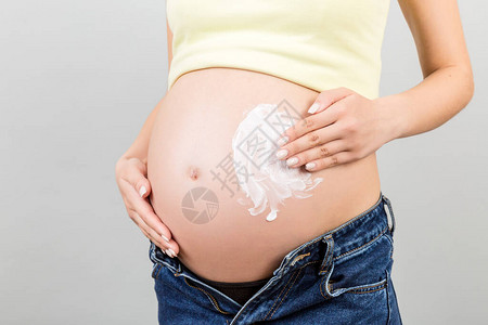 身穿无缝牛仔裤的孕妇在腹部施润湿乳油图片