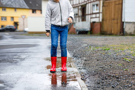小男孩穿着红色雨靴在雨夹雪和雨天行走的特写镜头穿着五颜六色便服的孩子跳进水坑在户外玩乐图片