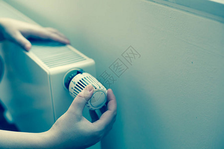 女青年手用温度控制器改变散热器温度的图片