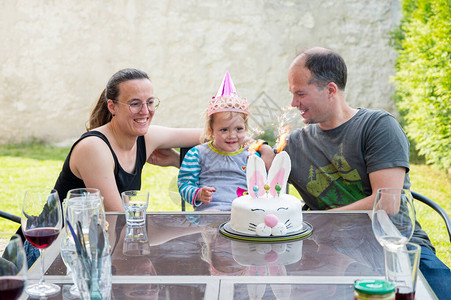 金发美女和爸妈一起庆祝生日家庭节日在户外兔子蛋糕上吹蜡烛图片