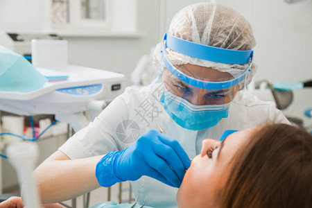 女牙医用蓝色手套和防护面罩治疗牙腔牙医在牙科诊所办公室进行龋齿治疗人医学口腔医背景图片