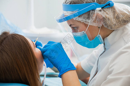 女牙医用蓝色手套和防护面罩治疗牙腔牙医在牙科诊所办公室进行龋齿治疗人医学口腔医图片