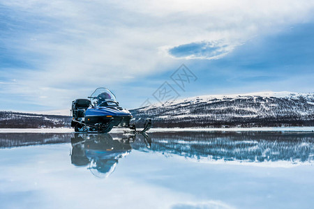 一辆蓝色雪车站在靠近开阔水域的冰冻湖泊上图片