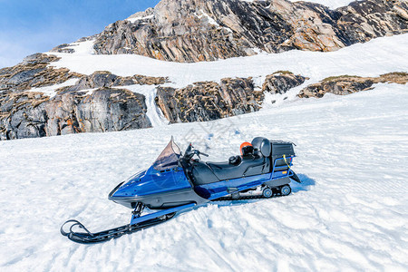 一辆蓝色雪地摩托站在靠近挪威山脉石头的雪地上图片