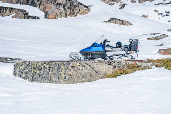 一辆蓝色雪地摩托站在靠近挪威山脉石头的雪地上图片