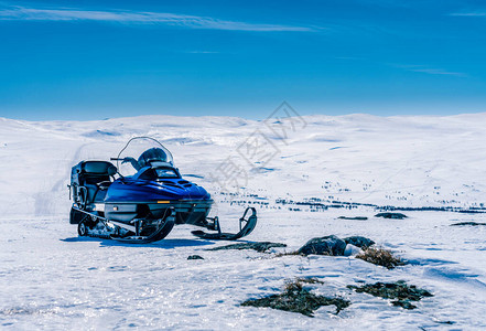 一辆蓝色的雪地摩托站在挪威山区的地壳雪上图片