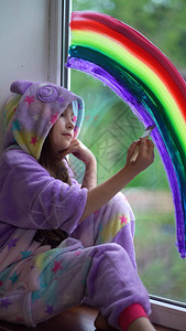 穿着睡衣的女孩在家里的窗户上画彩虹我从窗背景图片
