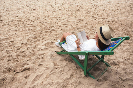 一个美丽的女人躺下躺在沙滩椅子上读书感图片