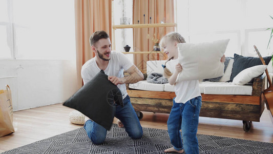 英俊的年轻男人和可爱的小姑娘在家地毯上玩枕头搏斗图片