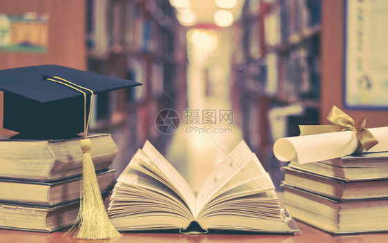 用毕业帽学术帽灰泥板和学位证书在课堂或图书馆学习室的书籍和教科书上图片