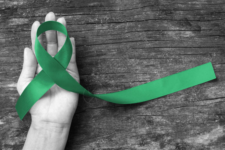 肝癌意识丝带翡翠绿丝带在人手老化背景上图片