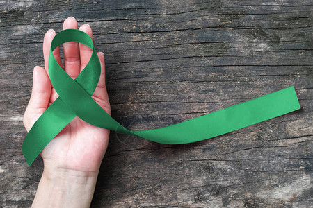 肝癌意识丝带翡翠绿丝带在人手老化背景上图片