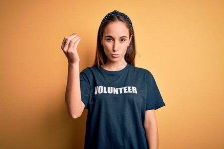 身穿志愿者T恤的年轻美女在黄色背景下做志愿者用手和指自信地表图片