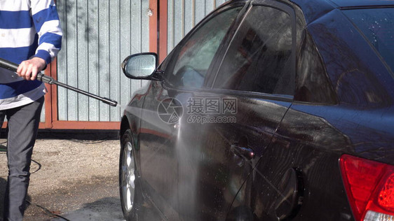 一名男子用高压水射流清洗汽车上的污垢洗车专用洗涤剂在家门口图片