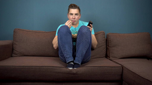 一个年轻人正在看电视和吃爆米花那家伙正在仔细地看电视电视剧情中的一个激动人心的时刻坐在沙发上电视上的景色看着图片