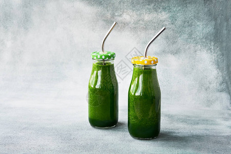两瓶小里装着菠菜的绿色冰淇淋灰色地底有金属稻草复制空间健康的图片